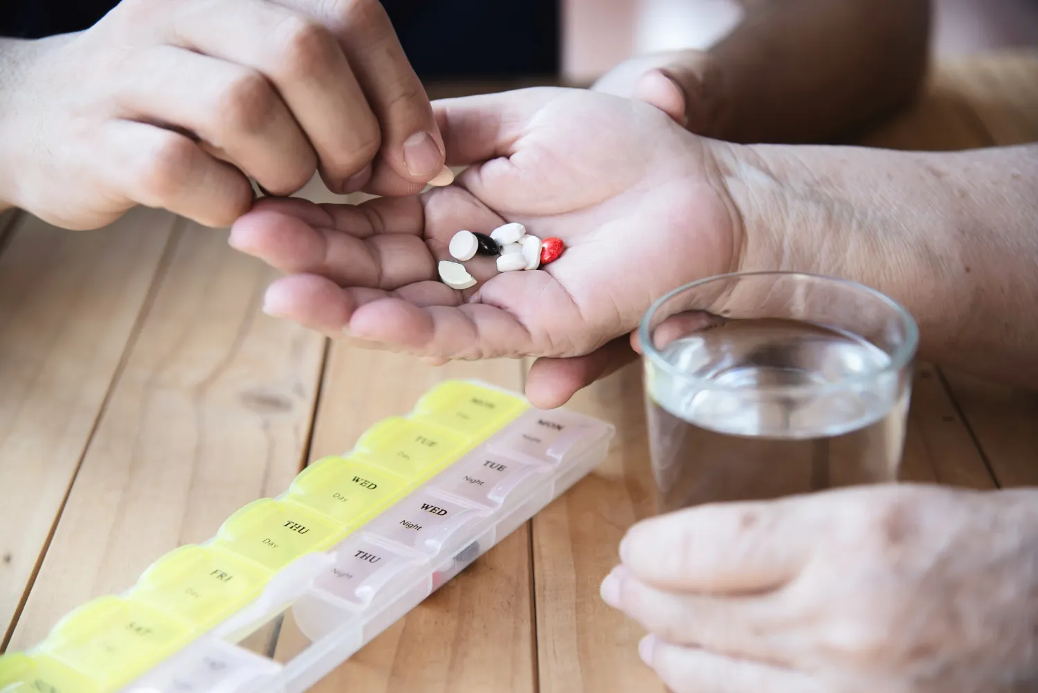 Caregiver organizing daily medications into a pill organizer and handing pills to an older adult as part of effective medication management to improve adherence and patient safety.