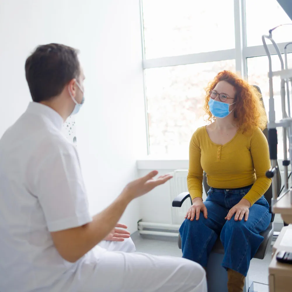 A masked healthcare professional discussing care with a patient during an appointment, highlighting personalized support, clear communication, and guidance throughout the treatment process.
