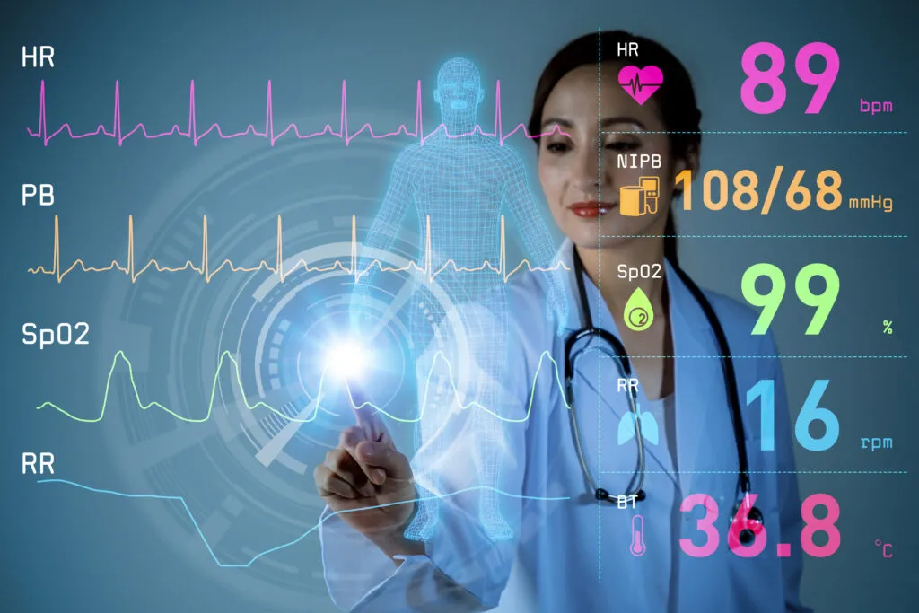 A female doctor in blue scrubs with a stethoscope touches a glowing digital health monitoring interface displaying real-time vital signs, including heart rate (89 bpm), blood pressure (108/68 mmHg), oxygen saturation (SpO2 99%), respiratory rate (16 rpm), and body temperature (36.8°C), alongside a translucent 3D human body outline and colorful waveform graphs, representing advanced digital patient monitoring technology.
