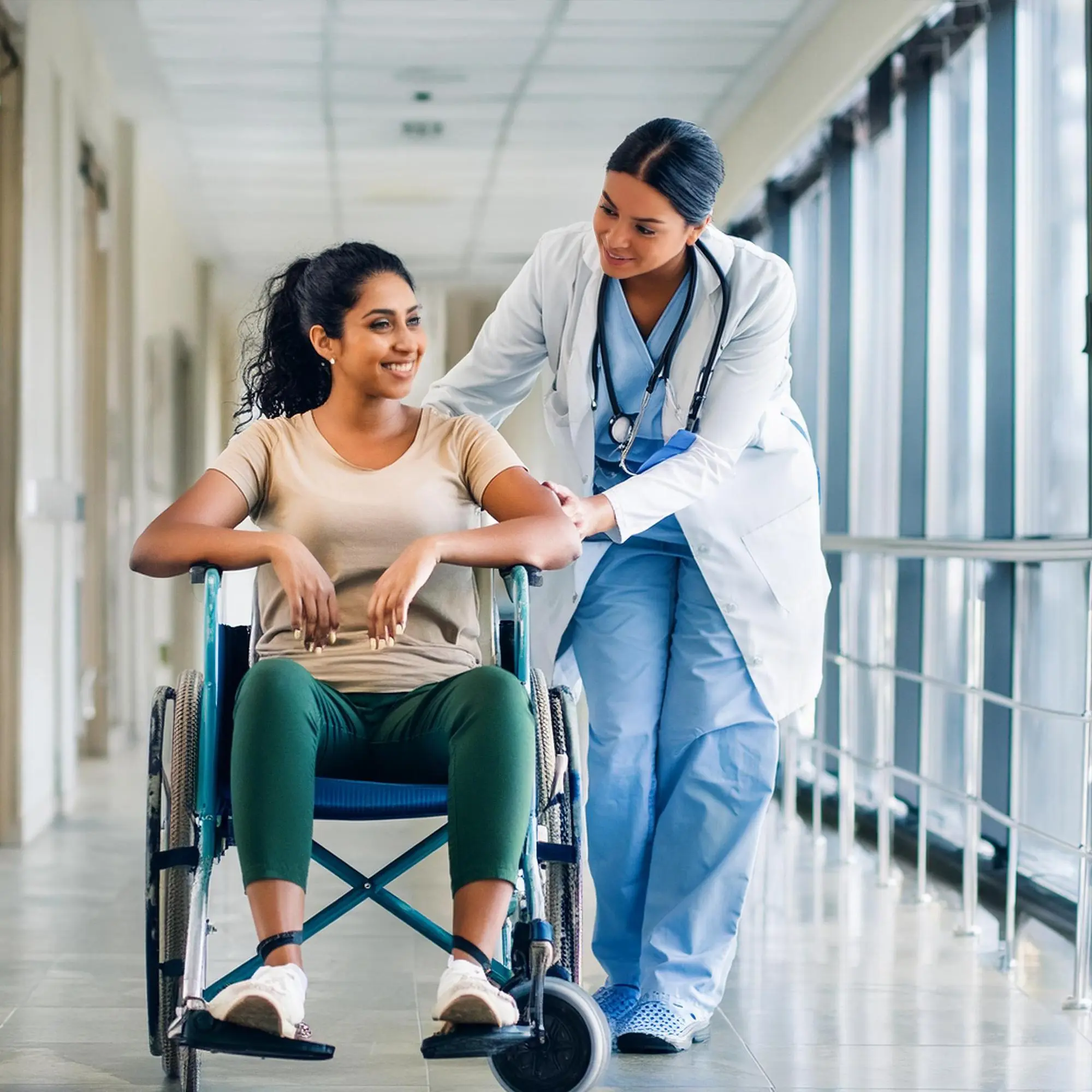 Nurse assisting a smiling patient in a wheelchair through a hospital corridor — Central Health Solutions transition care management and patient support services