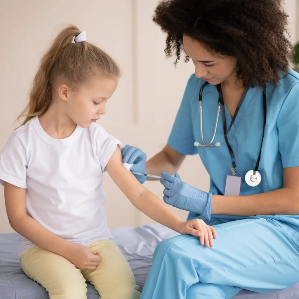 Healthcare professional in blue scrubs administering a vaccine to a young girl seated on an exam table in a bright clinic, illustrating safe, compassionate pediatric care and immunization services.
