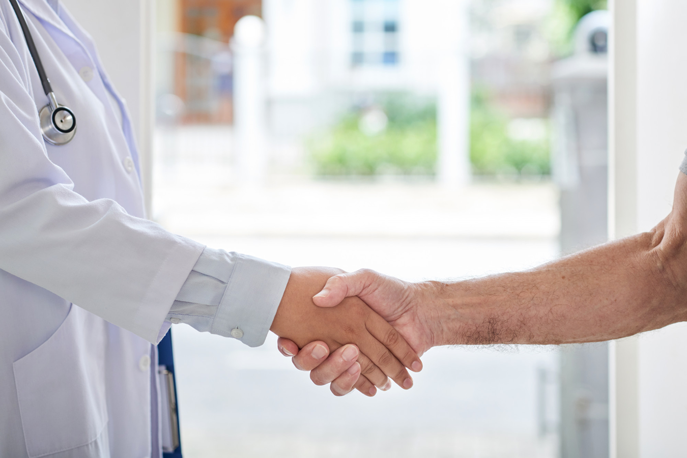 Medical professional in a white coat with a stethoscope shaking hands with a patient, conveying care and collaboration.