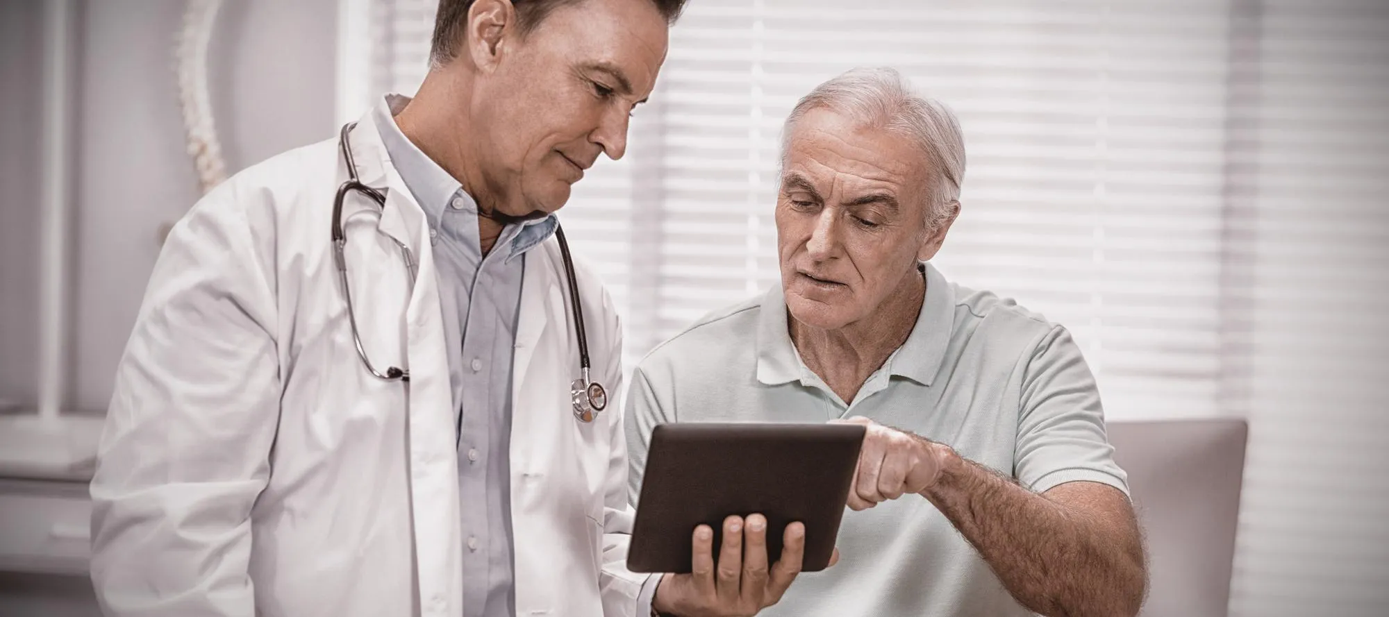 Doctor explains medical information to an older man using a tablet in a clinic setting
